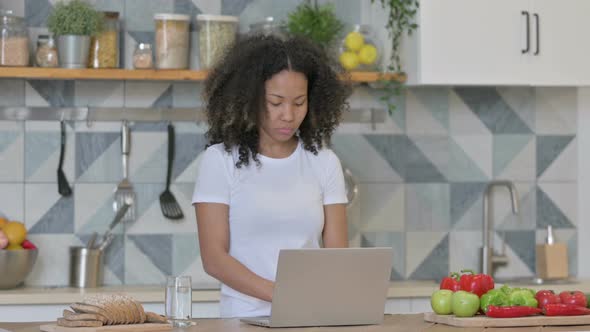 Young African Woman Working on Laptop in Kitchen