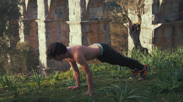 Young strong lean fit man doing push ups outdoors in sunshine within nature