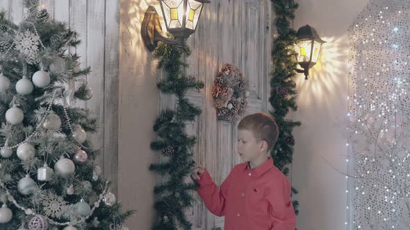 Blond Boy Child in Red Shirt Adjusts Pine Decor with Cones