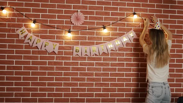 The Girl Decorates the Room for the Holiday with Garlands and Flags