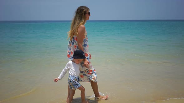 Mother and Son Walking on Foot Along the Beach Near the Ocean