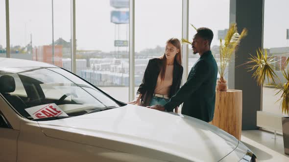 African Man and Caucasian Woman Choosing New Vehicle at Showroom