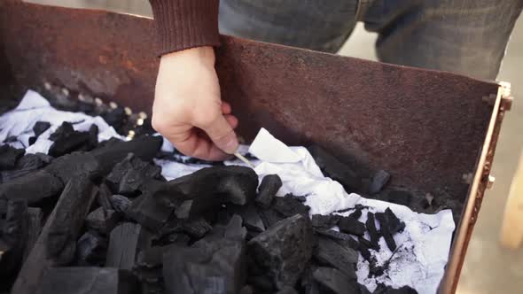 A Man Lights a Fire with Paper Matches and Coals