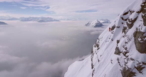 Aerial drone view of a skier skiing down a steep snow covered mountain