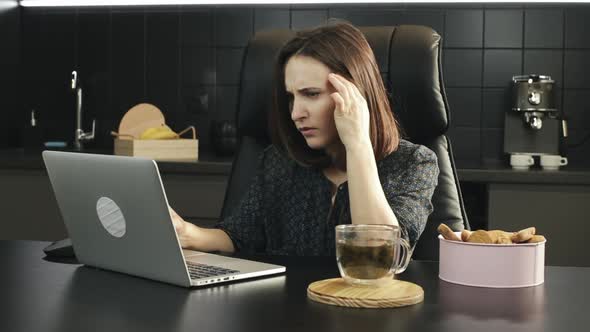 Young female freelancer with headache working on laptop computer at home. Stressed woman at work