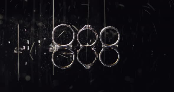 Wedding and Engagement Rings Lying on Dark Water Surface Shining with Light