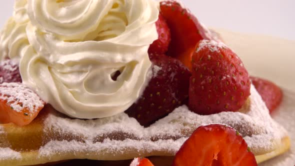 Belgian waffles with strawberry, whipped cream and powdered sugar on a plate on a white background.