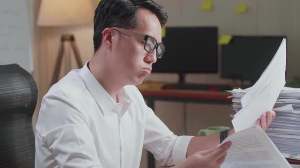 Close Up Of Asian Man Having Headache While Working Hard With Documents At The Office