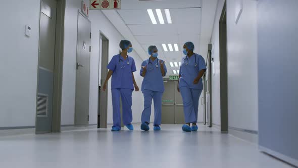 Diverse female doctors wearing face masks talking walking in hospital corridor