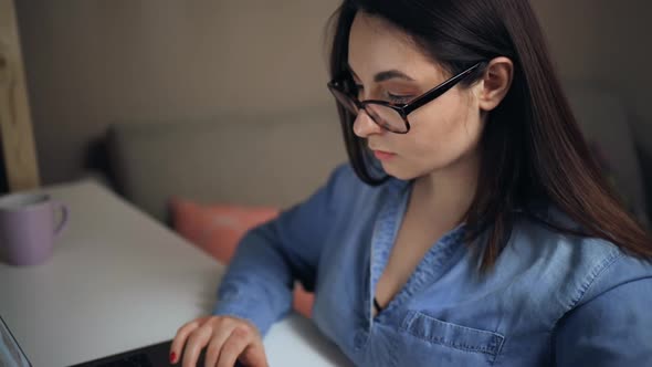 Serious Woman Concentrates and Looks at Laptop During Freelance Work at Home