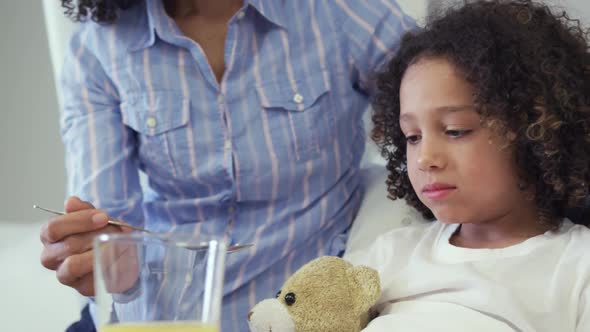 Front view of African american mother feeding her son food in bed in the ward at hospital 