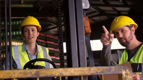 Workers sitting in forklift and talking to each other in warehouse