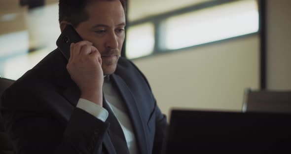 A man in a formal suit talking on the phone, while working at the office. Close up, slow motion.