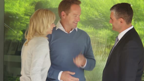 Mid Shot portrait of couple with estate agent in front of contemporary house, handing over the key