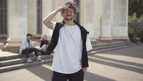 Portrait of Carefree Smiling Hippie Man in Sunglasses Shaking Dreadlocks Looking at Camera with