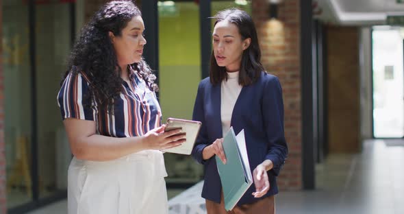 Two focused biracial businesswomen working together, using tablet in modern office