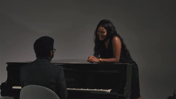 A Back View of a Young African American Musician Playing a Black Piano for His Beloved. Happy Woman