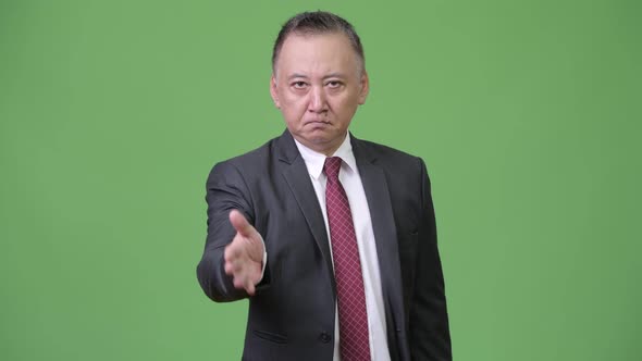 Mature Japanese Businessman Giving Handshake Against Green Background