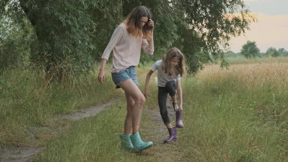 Two Happy Girls Sisters Walking After Rain in Dirty Clothes Fun Pouring Water From Their Boots