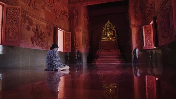 Asian woman prays in Buddhist temple sitting on floor