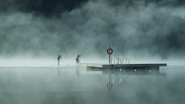 A Couple of Paddle Boarders Passing by a Wooden Diving Spot on a Foggy Lake