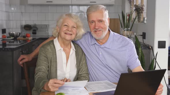 Portrait of a Happy Married Elderly Couple Sitting at a Desk and Laptop