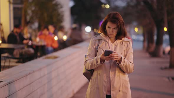 Woman Checking Smartphone on City Street