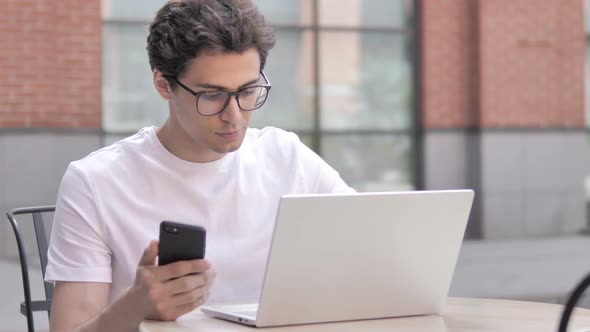 Young Man Using Smartphone and Laptop Outdoor