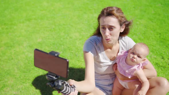 Mother Blogger with Little Daughter Having Fun Records a Video Blog on Green Grass