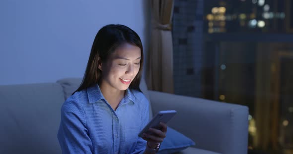 Woman use of mobile phone and sit on sofa at night