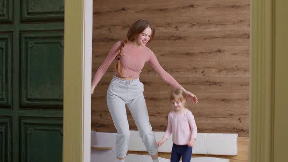 Young Lovely Mother Babysiter and Little Kid Daughter Jumping Dancing on Bed in Modern House Bedroom