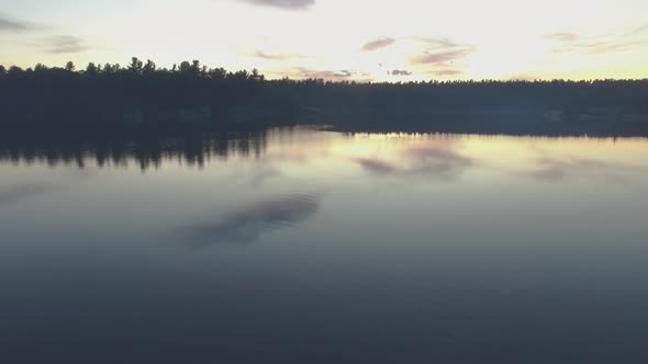 Aerial shot flying low over the still water of Charleston Lake in Ontario, Canada at sunset