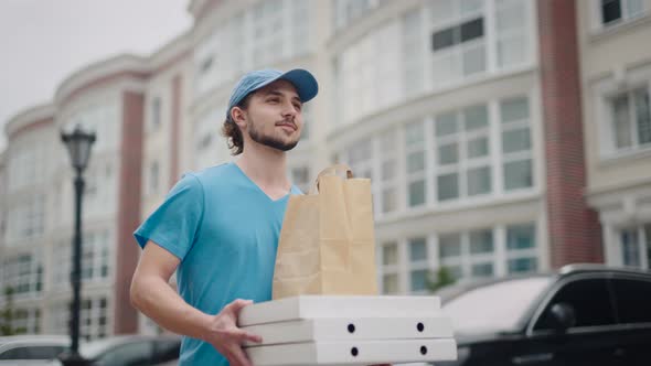 A Young Food Delivery Man Walks Through a Modern Pleasant Neighborhood