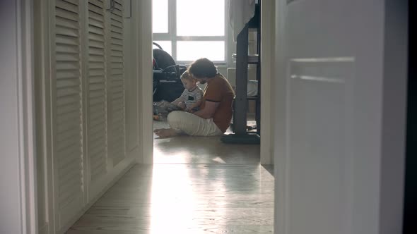 Alone Father Sitting on the Floor with His Baby Son and Reading a Book