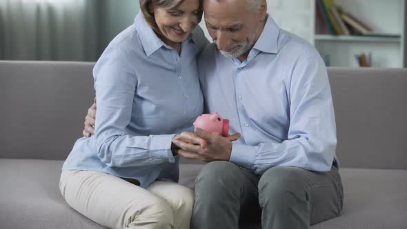 Retired Couple on Couch Holding Piggy Bank, Matured Paid out Insurance, Secure