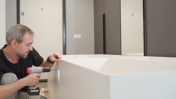 A Man Drills a Hole with an Electric Drill in a Cabinet