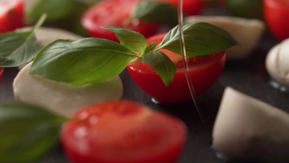 Camera follows pouring olive oil over tomato and mozzarella cheese salad. Slow Motion.