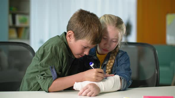 Children Entertainment Child with Felttip Pen Draws on Plaster Cast Boy Cares About Sick Female