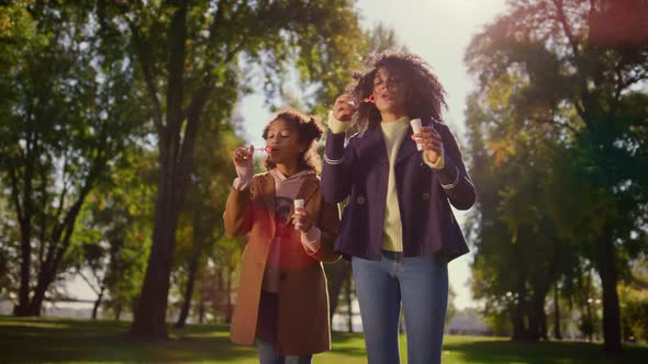 Joyful Family Blowing Soap Bubbles Standing in Green Park