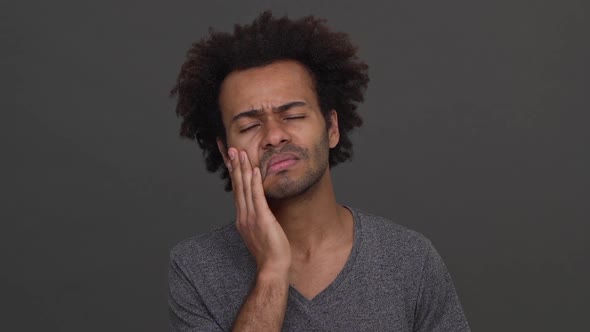 Dark Skinned Young Man Touching His Cheek Showing Toothache Isolated on Charcoal Background