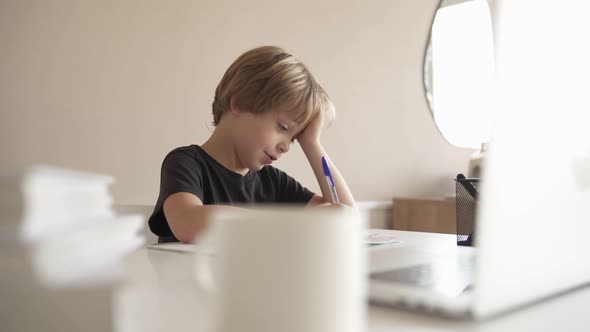 A Child Does Homework Using a Laptop While Sitting at Home in the Kitchen at the Table. Online