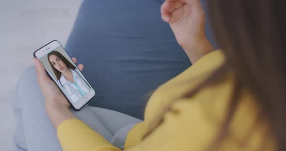 A Woman Lying on the Couch Talking To a Woman Doctor on Video Using a Smartphone. Remote Medical