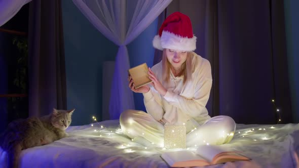 Excited Smiling Woman in Red Santa Christmas Hat Opens Gift Box with Magic Light