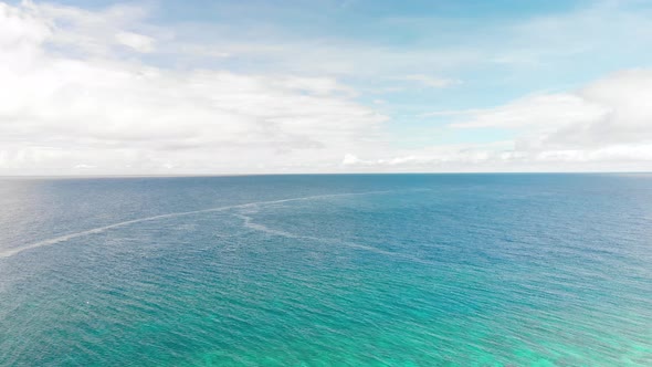 horizon drone footage of open blue turquoise tropical ocean under a sky with fluffy white clouds