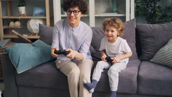 Emotional Girl Playing Video Games with Little Son Holding Joystick at Home