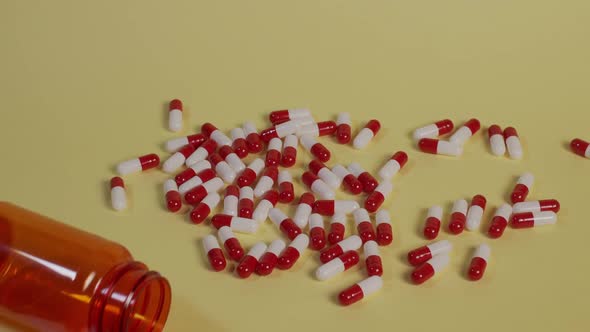 Slow motion high-angle medium shot of a pile of pills as an empty pill bottle falls vertically on th