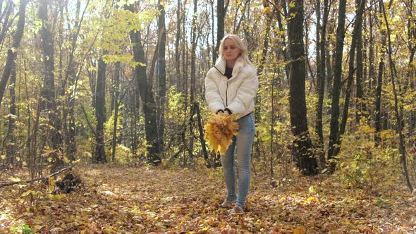 Blonde woman throws a bouquet of yellow leaves in the autumn forest. Slow motion.
