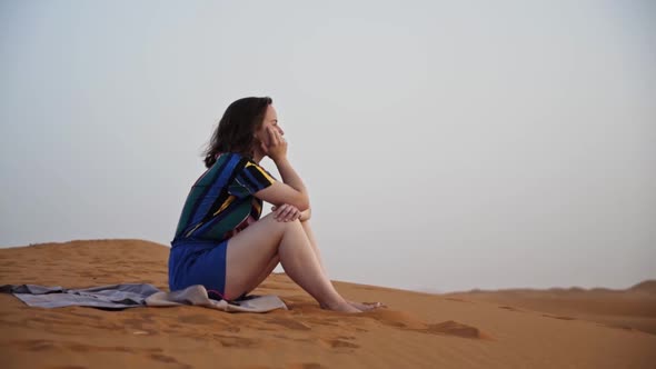 Young woman sitting in contemplation on the desert sands of the Sahara. Morocco.
