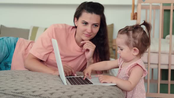 Baby and Mom Use Laptop at Home on Bed