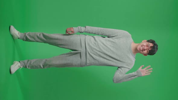 Full Body Of Asian Man Waving Hand And Smiling While Standing On Green Screen In The Studio